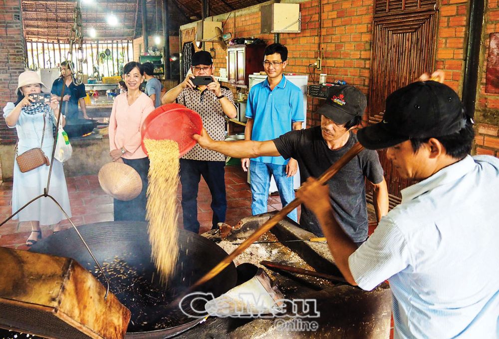 Du khách thích thú khi tận mắt xem những người thợ chế biến món cốm nếp, một trong những đặc sản của tỉnh Vĩnh Long.