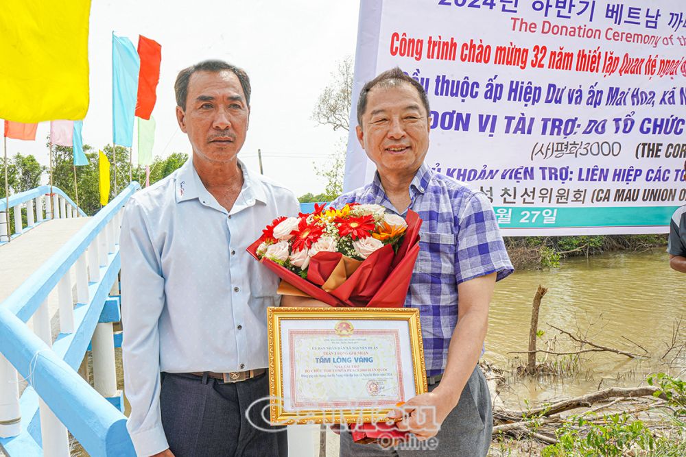 Ông Lục Minh Triều, Chủ tịch Uỷ ban MTTQ xã Nguyễn Huân, tặng hoa và bảng Tấm lòng vàng cho đại diện Tổ chức The Corea Peace3000.