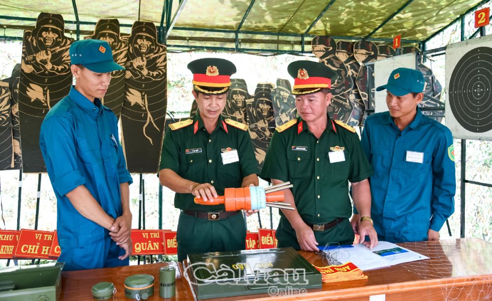 Thiếu tá Lê Việt Chiến (thứ hai từ trái sang phải), trợ lý Chính trị Ban CHQS huyện Thới Bình giới thiệu mô hình súng bắn Flaycam.