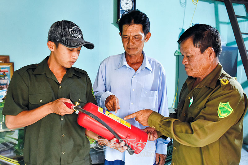 Ông Mai Tắc Long (bìa phải) tuyên truyền, hướng dẫn bà con tiểu thương trang bị bình chữa cháy.